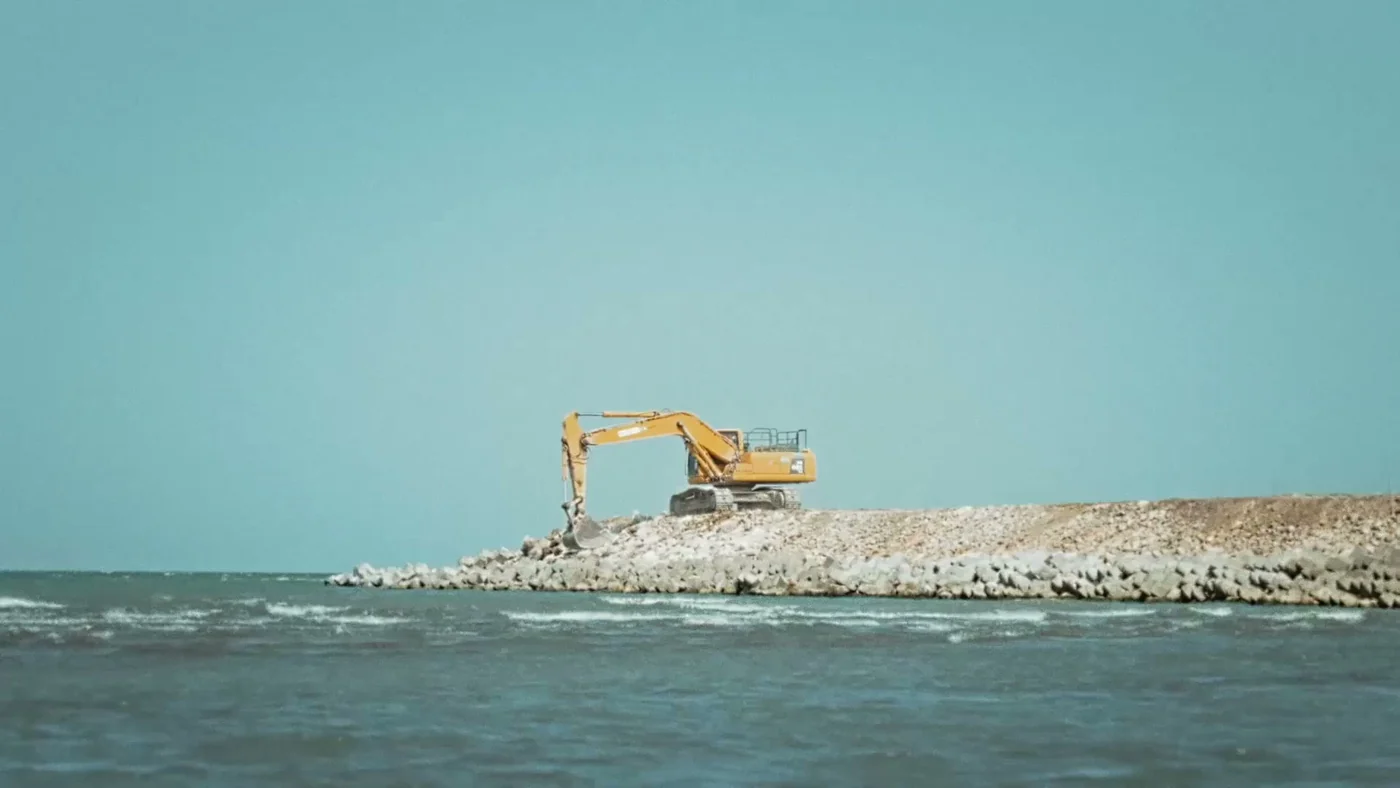 Экскаватор насыпает каменную дамбу в море — ранняя стадия намыва берега